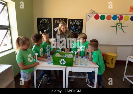 Female school teacher with a group of schoolchildren wearing green t shirts with a white recycling l Stock Photo