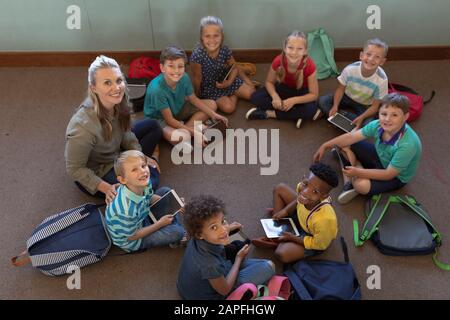 Female school teacher sitting cross legged on the floor in a circle with a group of schoolchildren i Stock Photo