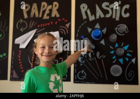 Schoolgirl wearing a green t shirt with a white recycling logo on it and it, pointing to a poster Stock Photo