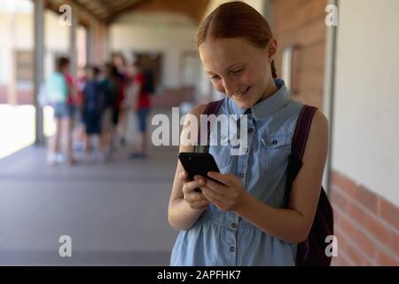schoolgirl standing in the schoolyard at elementary school using a smartphone Stock Photo