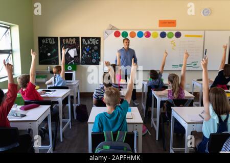 Male school teacher standing in an elementary school classroom with a group of school children Stock Photo