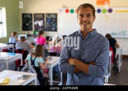 Male school teacher standing with arms crossed in an elementary school classroom Stock Photo