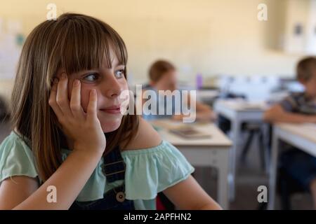 Schoolgirl sitting at a desk leaning her head on her hand in an elementary school classroom Stock Photo