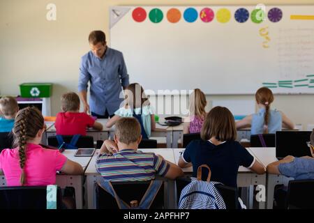 Male school teacher standing in an elementary school classroom with a group of school children