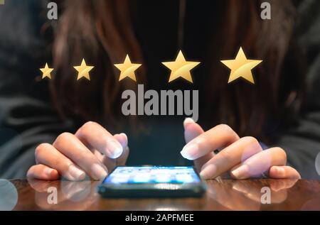 Woman filling out 5 star gold customer service feedback survey on electronic mobile device after online shopping experience - Business satisfaction ratings, retention and quality of service concepts Stock Photo