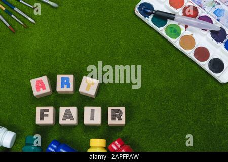 Art trade fair flat lay concept written on wood blocks on grass background - Creative overhead backdrop poster banner with artistic tools and copy space - Exhibition, shopping and painting concepts Stock Photo