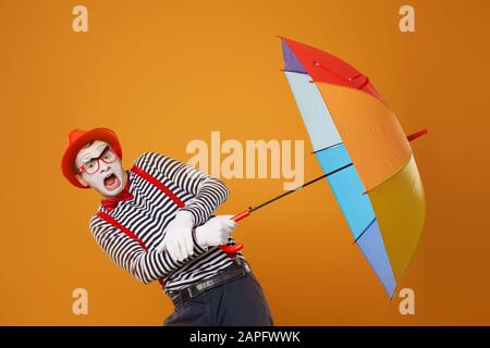 Mime with multi-colored umbrella isolated on blank orange background in studio Stock Photo