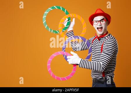 Happy mime man with multi-colored rings on empty orange background Stock Photo