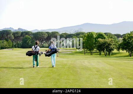 Friends carrying golf bag walking on golf course Stock Photo