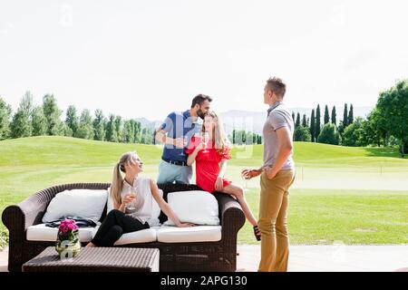 Friends enjoying wine and talking on sofa on golf course Stock Photo