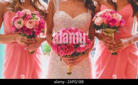 Midsection of bride and bridesmade in pink gownholding bouquet of flowers Stock Photo