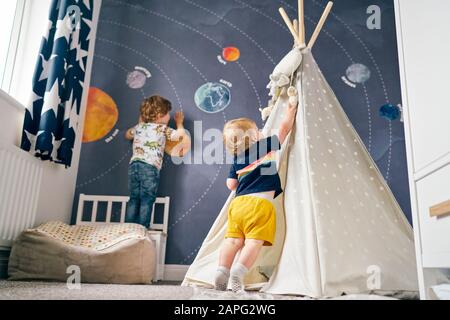 Brothers playing on mural of solar system and playing in teepee at home Stock Photo