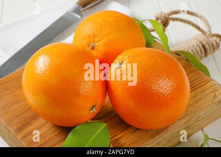 Three whole ripe oranges and leaves on cutting board Stock Photo