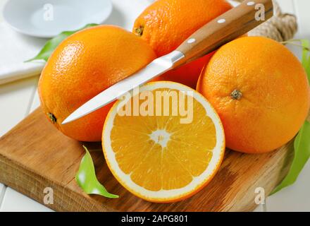 Three whole ripe oranges and a half on cutting board Stock Photo