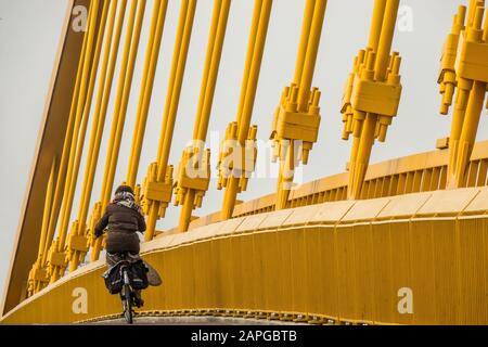 Man dressed in black riding a bicycle next to a wall made of yellow metal Stock Photo