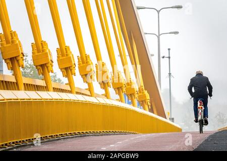 Man dressed in black riding a bicycle next to a wall made of yellow metal Stock Photo