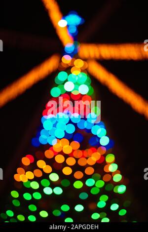 Christmas tree Blurred image with multicolored lights and garlands out of focus over dark night background. Stock Photo