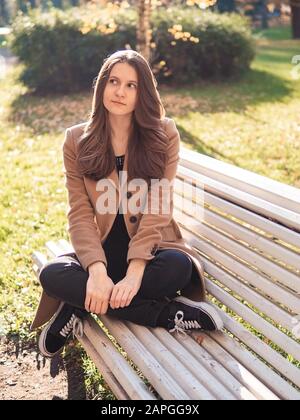 Beautiful teen girl sitting in the Park on a bench, dreaming, thinks. Woman with long hair Stock Photo