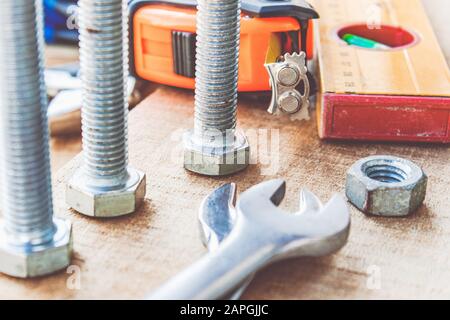 Steel bolt nuts and washers lie on wooden boards near an adjustable spanner and a tape measure. The concept of tools and repair work. Stock Photo