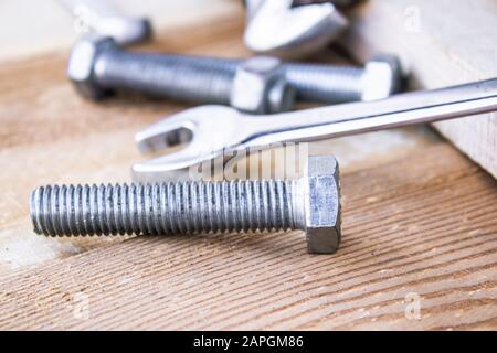 Steel bolts and nuts lie on wooden boards next to an adjustable wrench. The concept of tools and repair work. Stock Photo