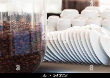 White ceramic saucers and small espresso cups stacked on the upper shelf of professional coffee machine, close-up photo with selective focus Stock Photo