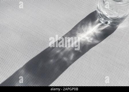 Abstract sunlight refraction pattern illuminates shadow of a standard glass on a table in a restaurant, top view Stock Photo