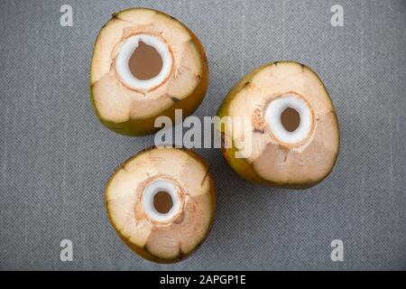 Three juicy green coconuts with holes for straw stand on a gray surface, flat lay photo, top view Stock Photo