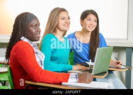 Three multicultural girls sit in class at school using laptop computer Stock Photo