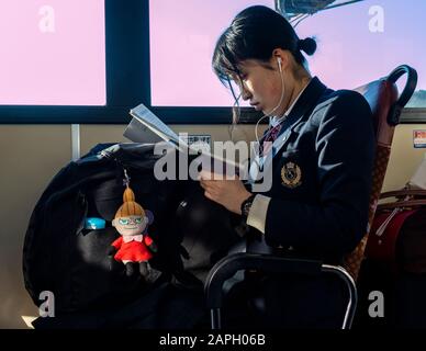 Kyoto, Japan - November 7th, 2018: A high school girl in her school uniform, reading on a bus in Kyoto, Japan.