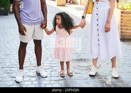 Happy multiethnic family from USA on their European vacation trip. White mother and black father holding hands with their mixed race daughter making f