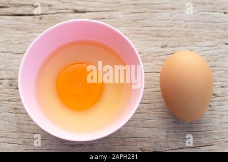 Broken egg shells and raw egg in small bowl  at wooden background for menu and recipe Stock Photo