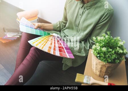 woman sitting on the floor in the room and choosing paint color from samples for new interior design Stock Photo