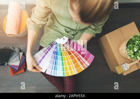 woman sitting on the floor in the room and choosing paint color from swatch for new interior design Stock Photo