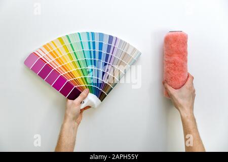 color swatch and paint roll in hands on white wall background Stock Photo