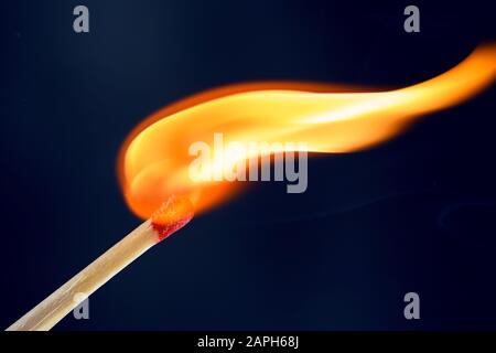 Match stick ignited burning bright big fire flame with smoke on dark background. Stock Photo