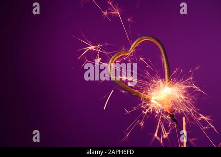 Burning sparkler in love heart shape on a purple background with lots of sparks. Valentine's day celebration. Stock Photo