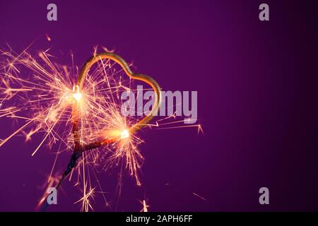 Sparkler in love heart shape on a purple background with lots of sparks. Wedding or Valentine's day celebration banner with copy-space.. Stock Photo