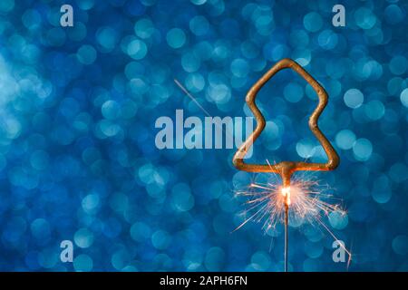 Burning sparkler in christmas tree shape on blue glitter background with copy-space. Stock Photo