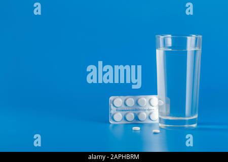 Glass with water and various pills isolated on blue background with copy space Stock Photo