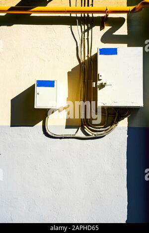 Electrical switchboard on the wall. Hard shadows. Wiring to the electrical panel on the wall. Detail of the cityscape. Grey wall Stock Photo