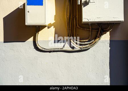 Electrical switchboard on the wall. Hard shadows. Wiring to the electrical panel on the wall. Detail of the cityscape. Grey wall Stock Photo