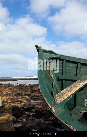 Top of green wooden fishing boat wreck stranded on beach with reef rocks, tide out . Stock Photo
