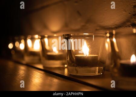 Line of votive candles and tea lights in a row with candlelight Stock Photo