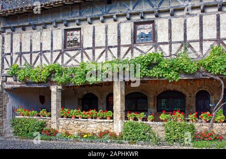 old half-timbered building, covered patio, leaded glass windows, potted red geraniums, flowers, grape vine, cobblestone street, medieval walled villag Stock Photo