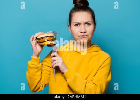 the girl shows discontent, measuring the height of the burger with a caliper on the side of herself, close up Stock Photo