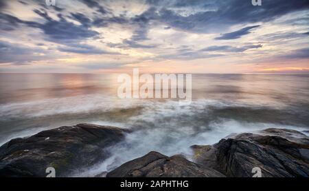 Scenic sunset over water seen from rocky shore, long exposure picture. Stock Photo