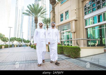 Middle-eastern young adults wearing kandora walking outdoors in Dubai - Two businessmen meeting outdoors Stock Photo