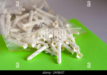 Screws with plastic dowels on a green background. A large set of fasteners in a plastic bag with a zip lock. Eye level shooting. Selective focus Stock Photo