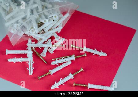 Screws with plastic dowels on a red background. Group fasteners in a plastic bag with a zip lock. Eye level shooting. Selective focus Stock Photo