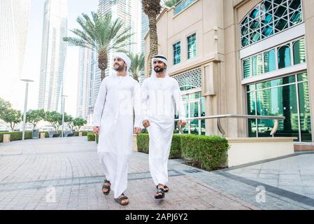 Middle-eastern young adults wearing kandora walking outdoors in Dubai - Two businessmen meeting outdoors Stock Photo